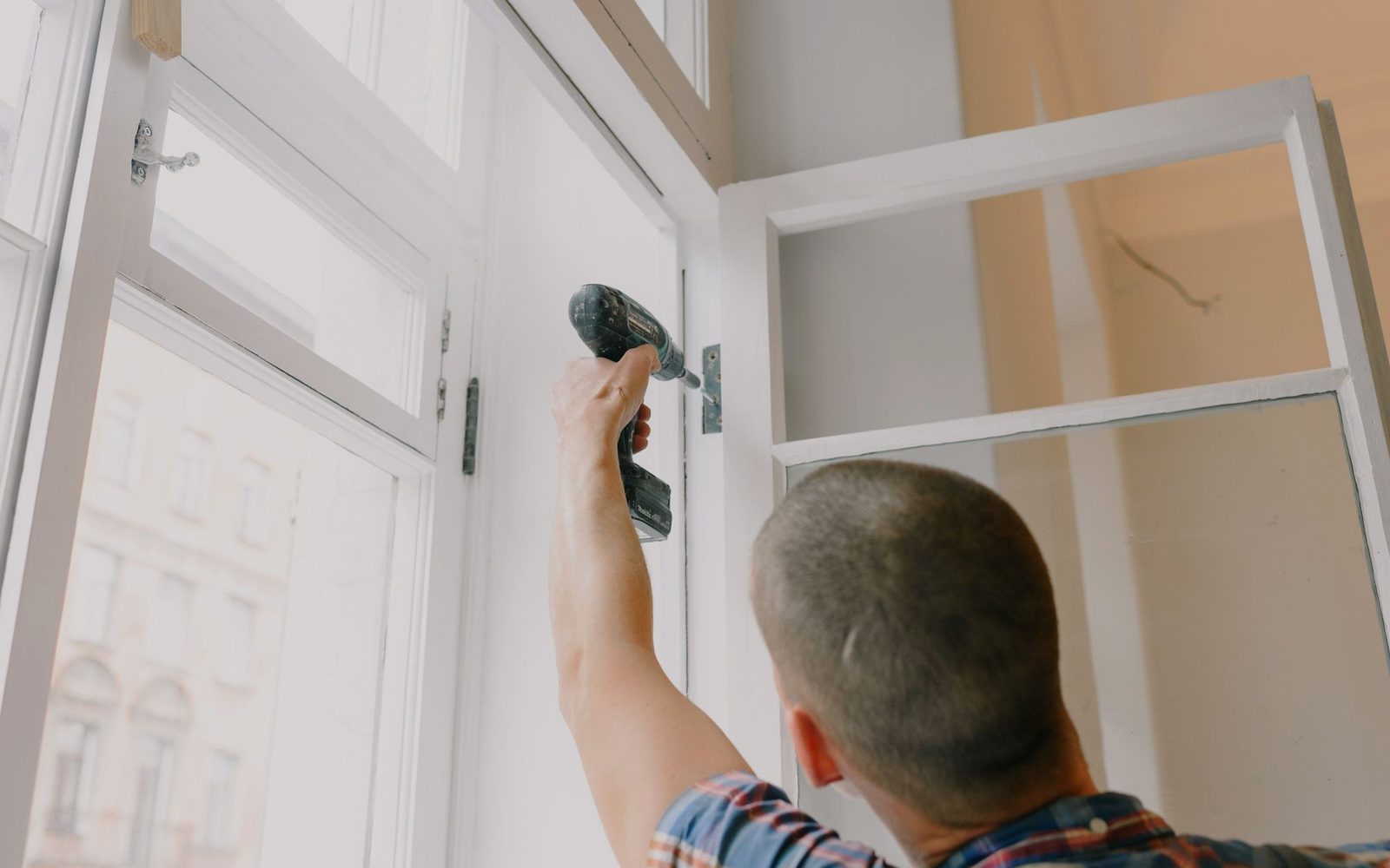 Worker fixing a door hinge with a cordless screwdriver