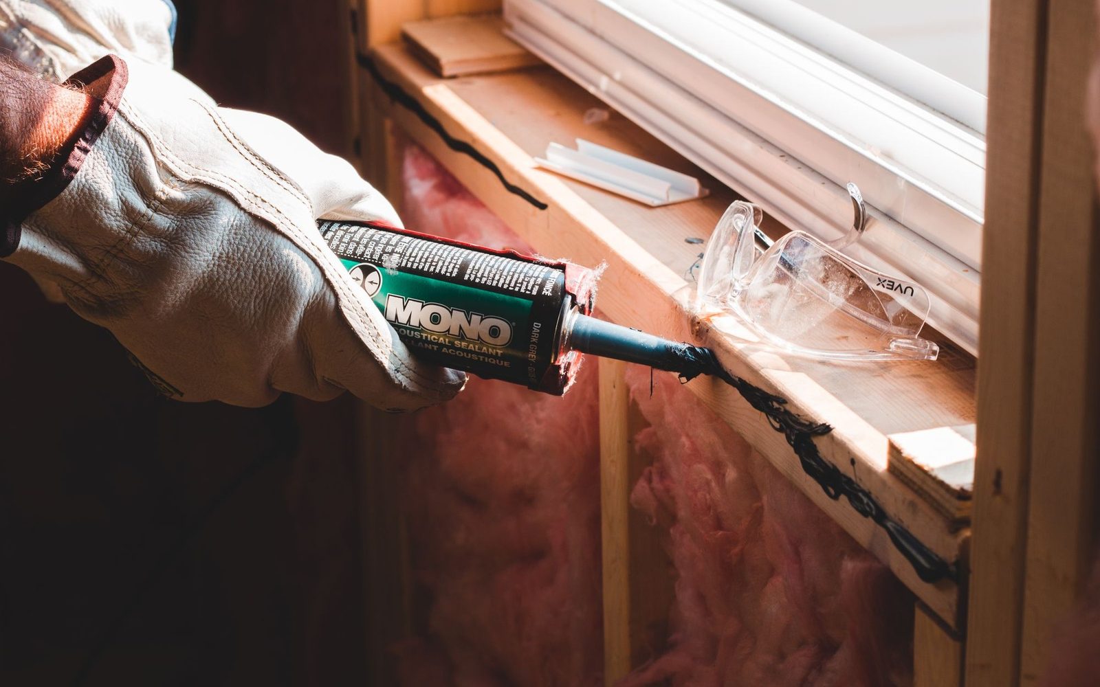Gloved hands applying sealant with a caulking gun
